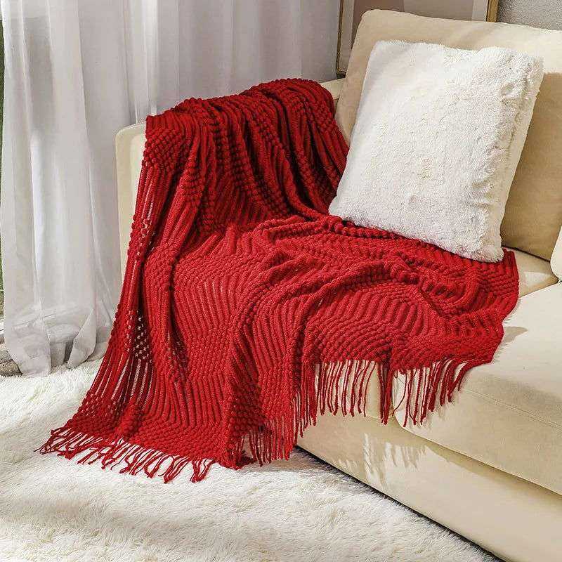 Knitted red blanket with tassels on a couch, part of a 10-color collection.