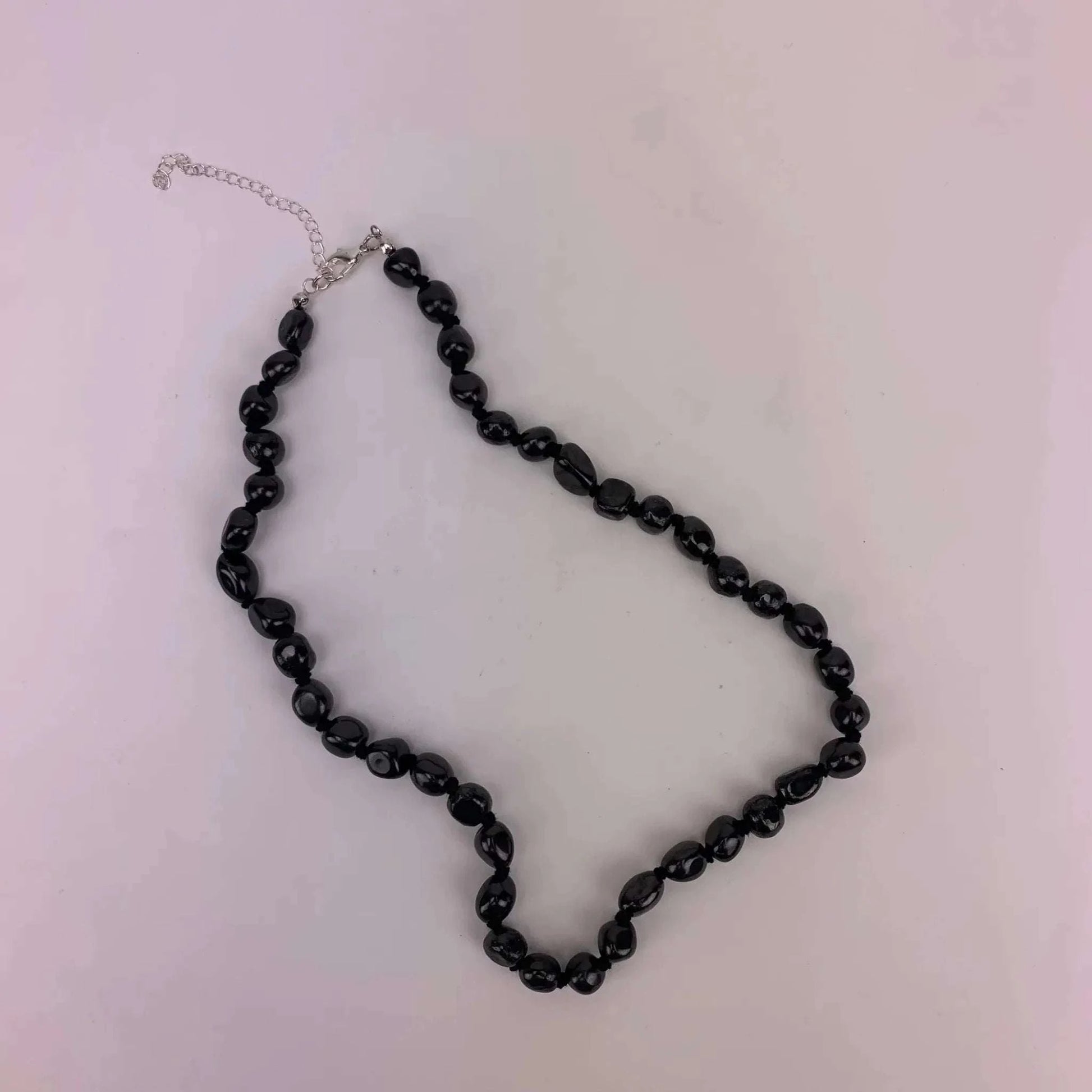 Shungite tumbled bead necklace with 7-10 mm stones on white background.
